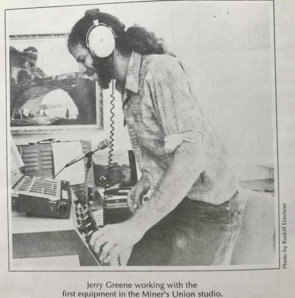 A man with headphones operates audio equipment in a studio. A framed picture of a bridge is on the wall. He is wearing a checkered shirt and jeans. Text reads: Jerry Greene working with the first equipment in the Miners Union studio.